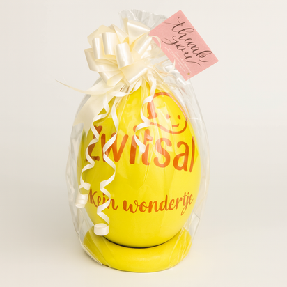 Een felgeel, ei-vormig Zwitsal geschenk met oranje opdruk “Klein wondertje” en wit lint bovenaan, geplaatst op een bijpasse