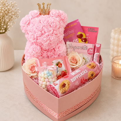 Roze hartvormige cadeaubox met rozenbeer, Yogurette, koekjes en snoep, feestelijk verpakt in transparante folie met roze strik.