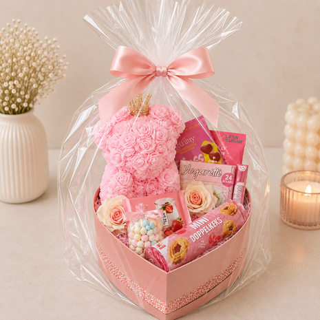 Roze hartvormige cadeaubox met rozenbeer, Yogurette, koekjes en snoep, feestelijk verpakt in transparante folie met roze strik.